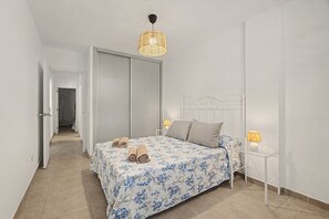 A bedroom with a bed, two bedside lamps, a hanging light fixture, and a door leading to a hallway. - Holiday Apartment 'Los Playeros' with Balcony and Wi-Fi (Arona)