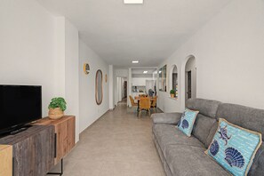 A modern living room with a flat-screen TV, a sofa with decorative pillows, and a dining area with a table and chairs. - Holiday Apartment 'Los Playeros' with Balcony and Wi-Fi (Arona)