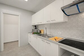 A modern kitchen with white cabinets, a stainless steel sink, and a black induction cooktop. - Holiday Apartment 'Los Playeros' with Balcony and Wi-Fi (Arona)