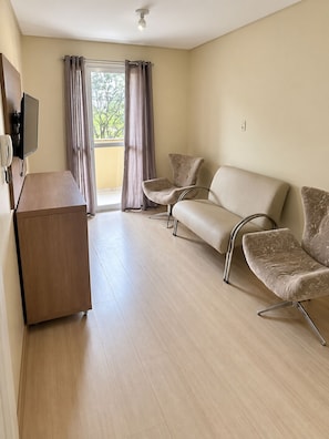 A hotel room with a wooden desk, two sofas, and a large window with curtains. - Apartamento com sacada prox a FAG (Cascavel)