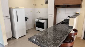 Una cocina compacta con encimera de granito, un refrigerador, una estufa y un lavamanos.
