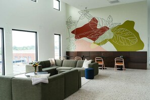 A modern lounge area with a sectional sofa, a small round table with a vase, and a wall mural. - Landing Modern Studio, Gym (Charlotte)