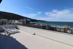 A rooftop terrace with lounge chairs, a view of the sea, and buildings in the background. - Penthouse with sea view in Bombas (Bombinhas)