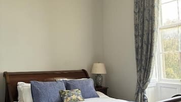 A bedroom with a wooden bed, a nightstand with a lamp, and a window with curtains.