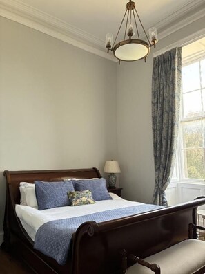 Une chambre avec un lit en bois, une table de chevet avec une lampe et une fenêtre avec des rideaux.