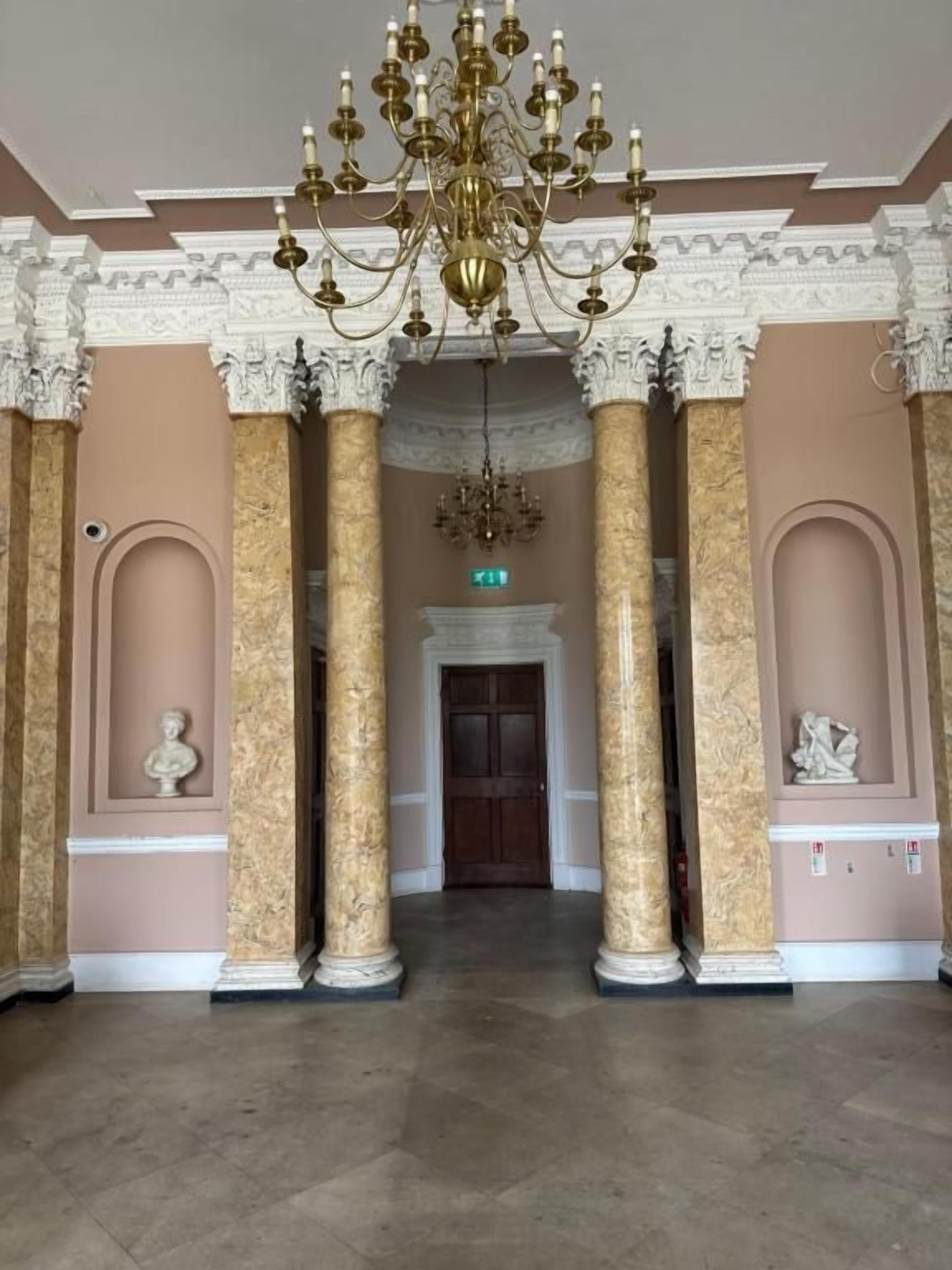 Ein prachtvoller Saal mit Marmorsäulen, einem Chandelier und einer Tür am Ende.