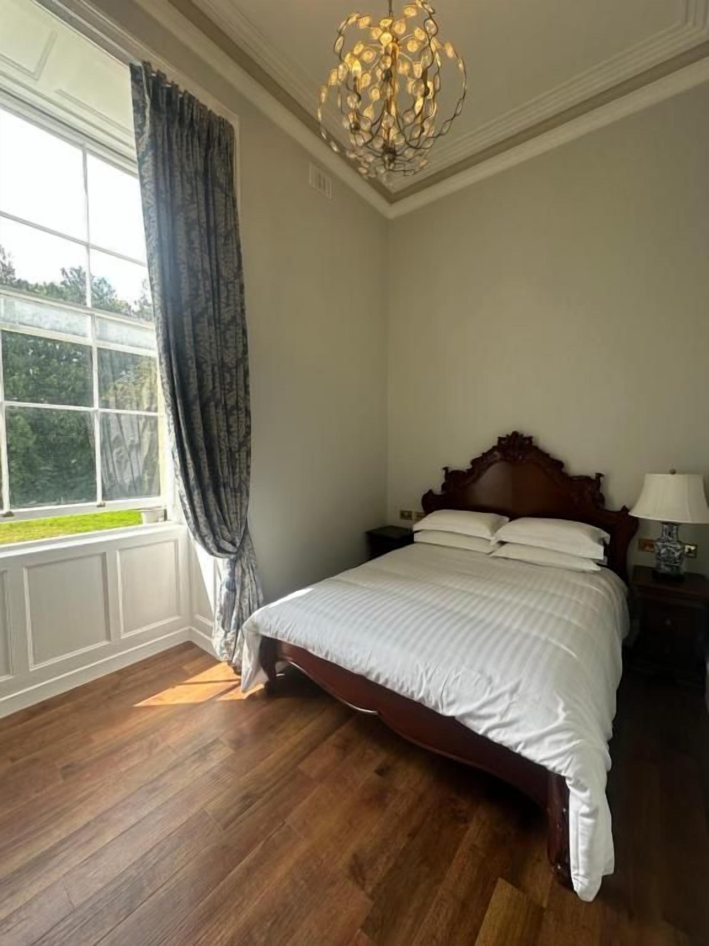 Un dormitorio con cama de madera, mesita de noche, lámpara y ventana con cortinas.