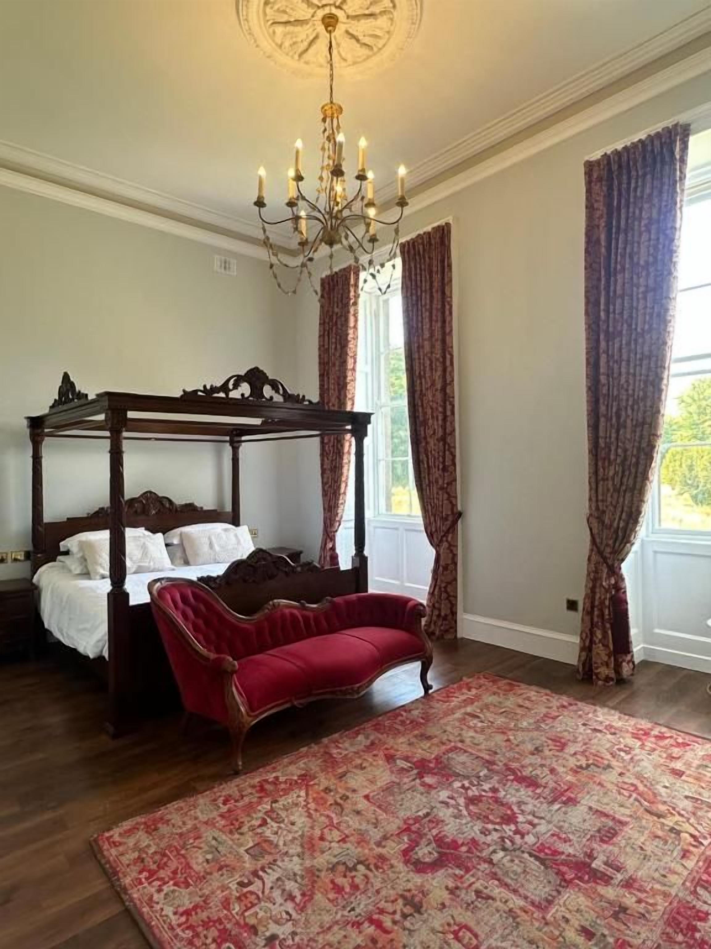 Une chambre à coucher avec un lit à baldaquin, un canapé rouge, un lustre et un tapis à motifs.
