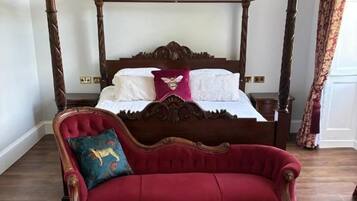 A four-poster bed with a red upholstered sofa in front, a patterned rug, and a wooden floor.