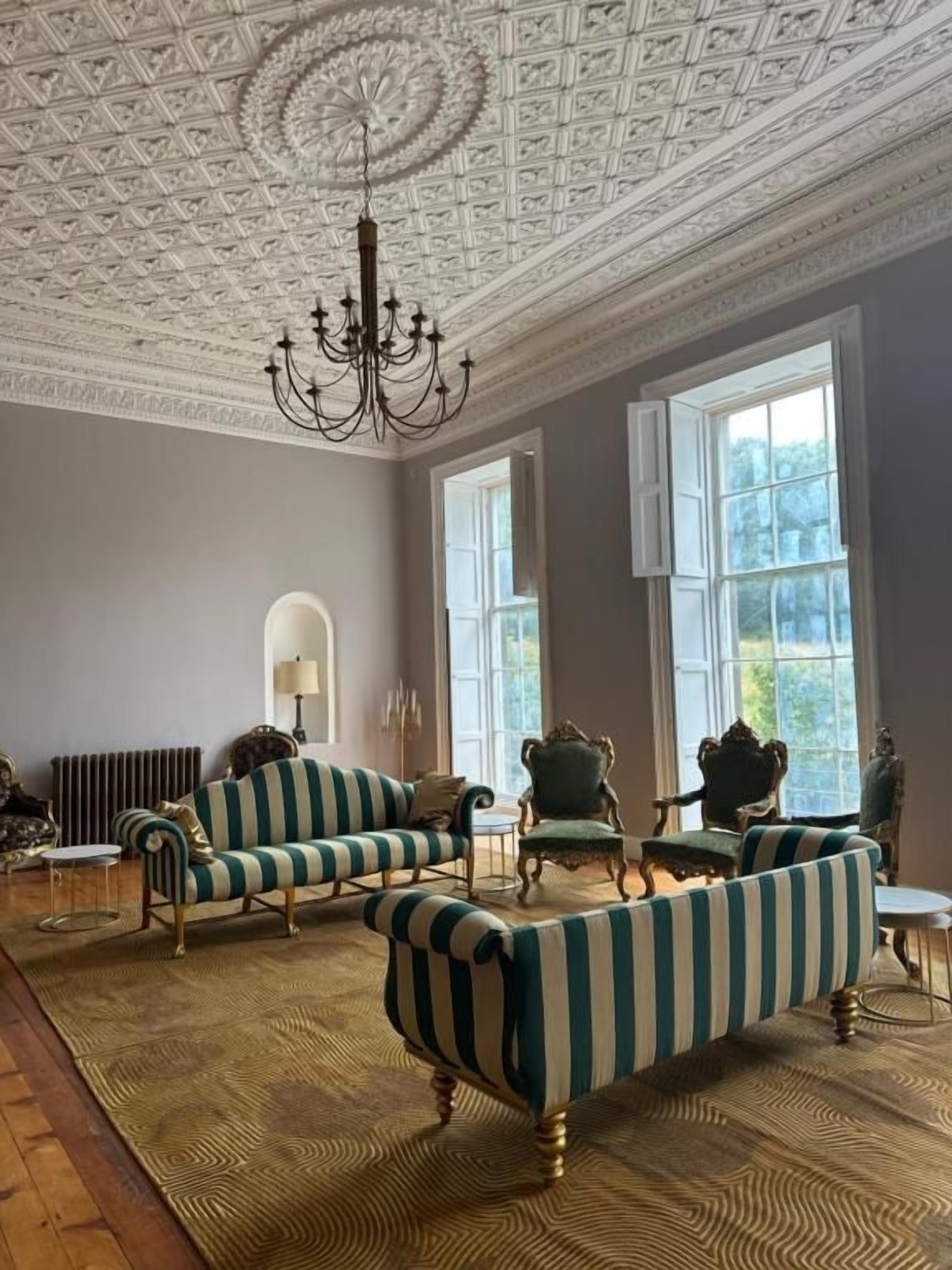 A room with striped sofas, a chandelier, and large windows.