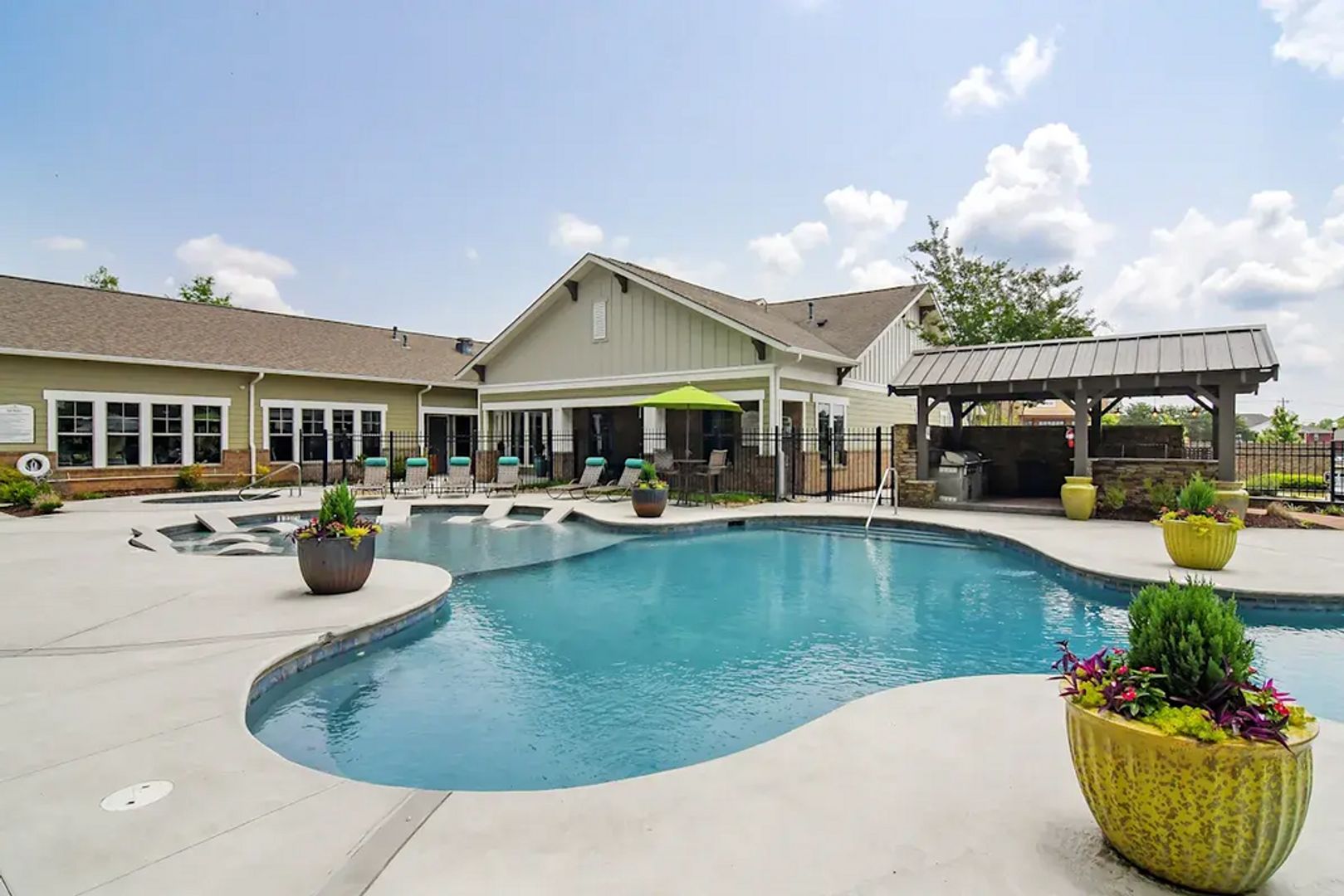 A swimming pool with a curved edge, surrounded by lounge chairs and planters, with a building in the background.