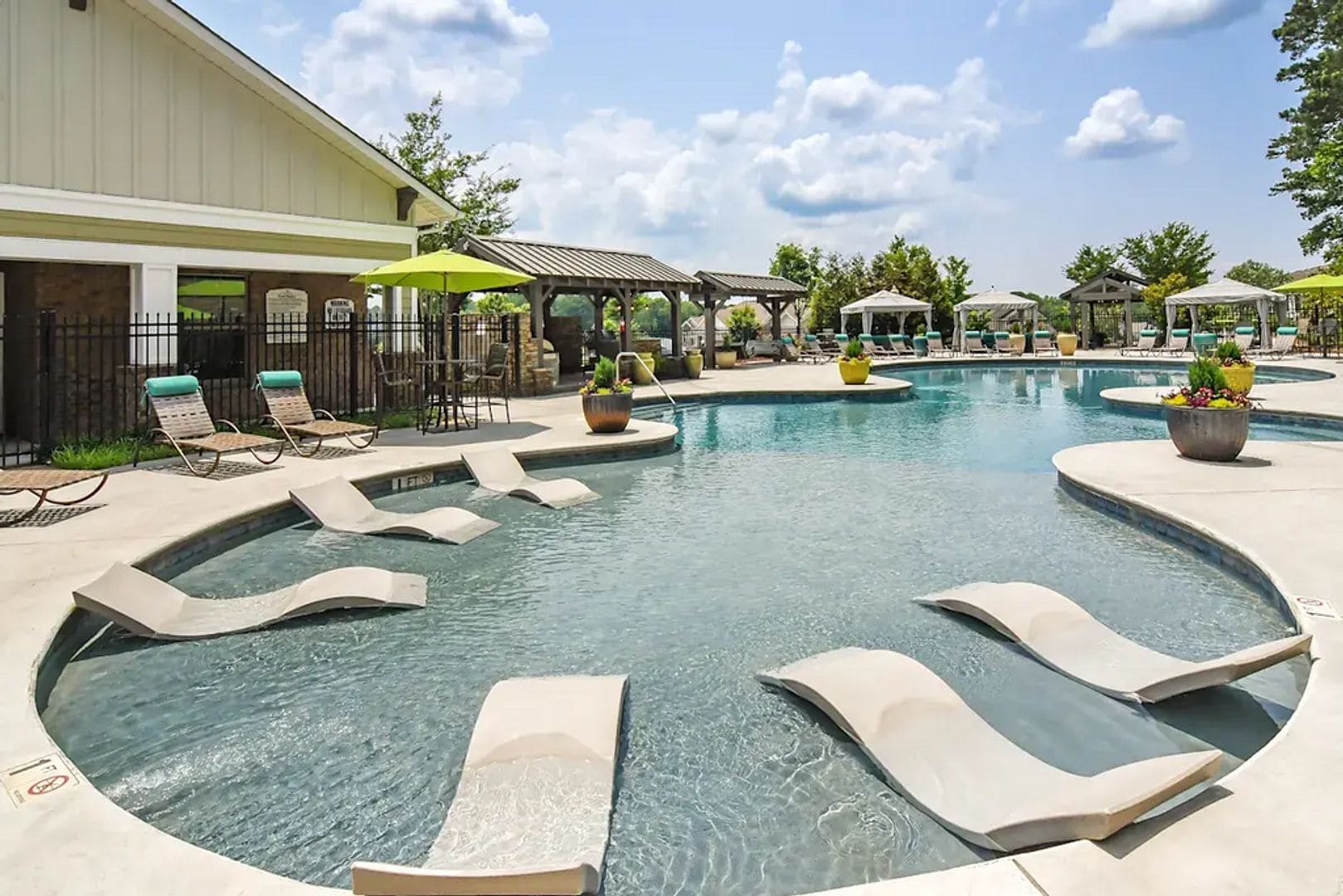 A pool area with lounge chairs, a gazebo, and a building with a sign.