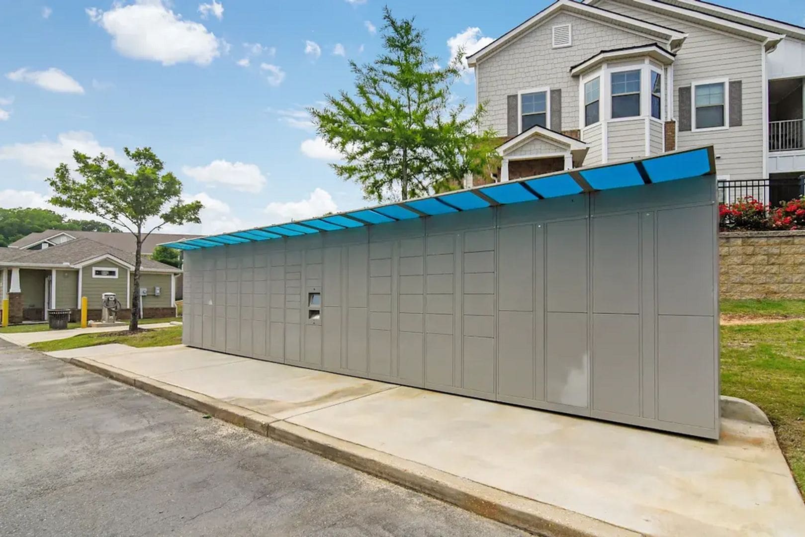 A grey utility building with a blue roof, located in a residential area with houses and trees.