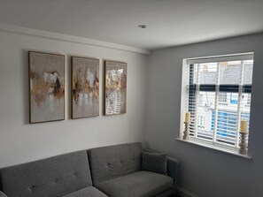 A room with a grey sofa, a window with blinds, and three abstract paintings on the wall.