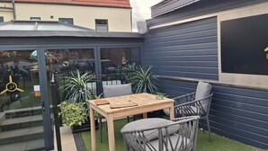 A patio area with a table and chairs, a logo for 'the Lancaster Lounge' on a wall, and a small garden with plants. - One-Bed Luxurious apartment near A1 (Yaxley)