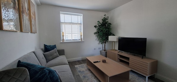 A living room with a sofa, a coffee table, a television, and a potted plant.