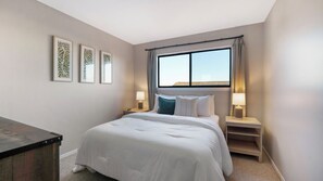 A hotel room with a large bed, two bedside tables with lamps, a window with curtains, and three framed wall art pieces. - Lakefront• Stunning Views • Free Boat Slip (Osage Beach)