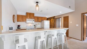 A kitchen with wooden cabinets, a white countertop, a stainless steel refrigerator, and a bar stool seating area. - Lakefront• Stunning Views • Free Boat Slip (Osage Beach)