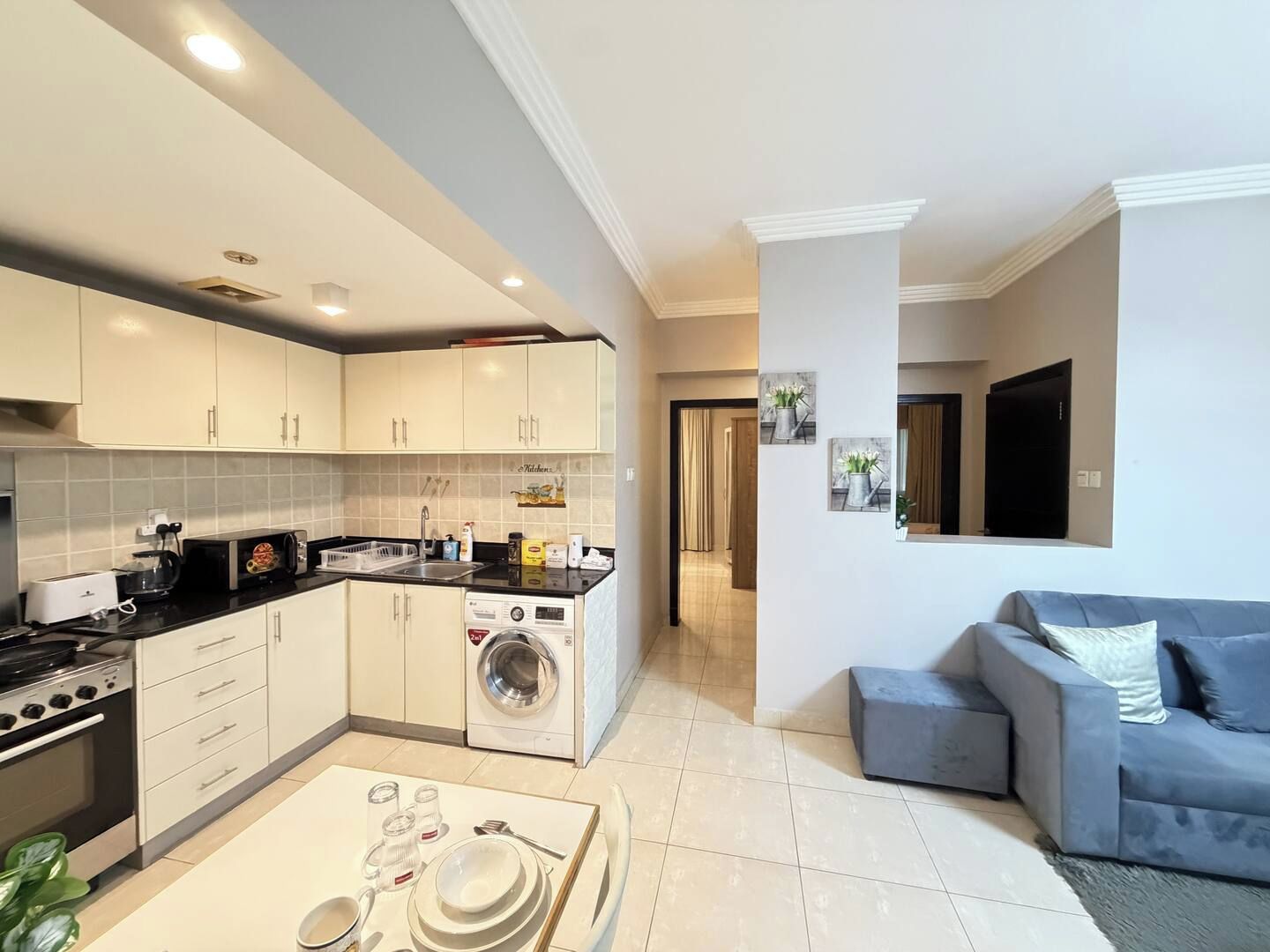 Una cocina moderna con lavadora integrada, un comedor con mesa para dos personas y un sofá gris en la sala de estar.