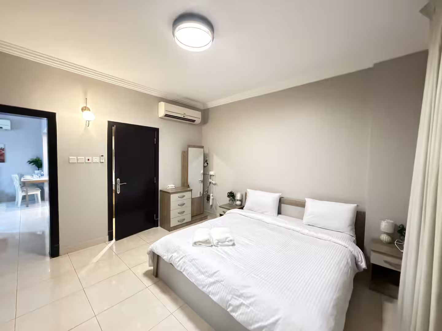 A modern bedroom with a large bed, bedside tables, a wardrobe, and a bathroom visible through an open door.