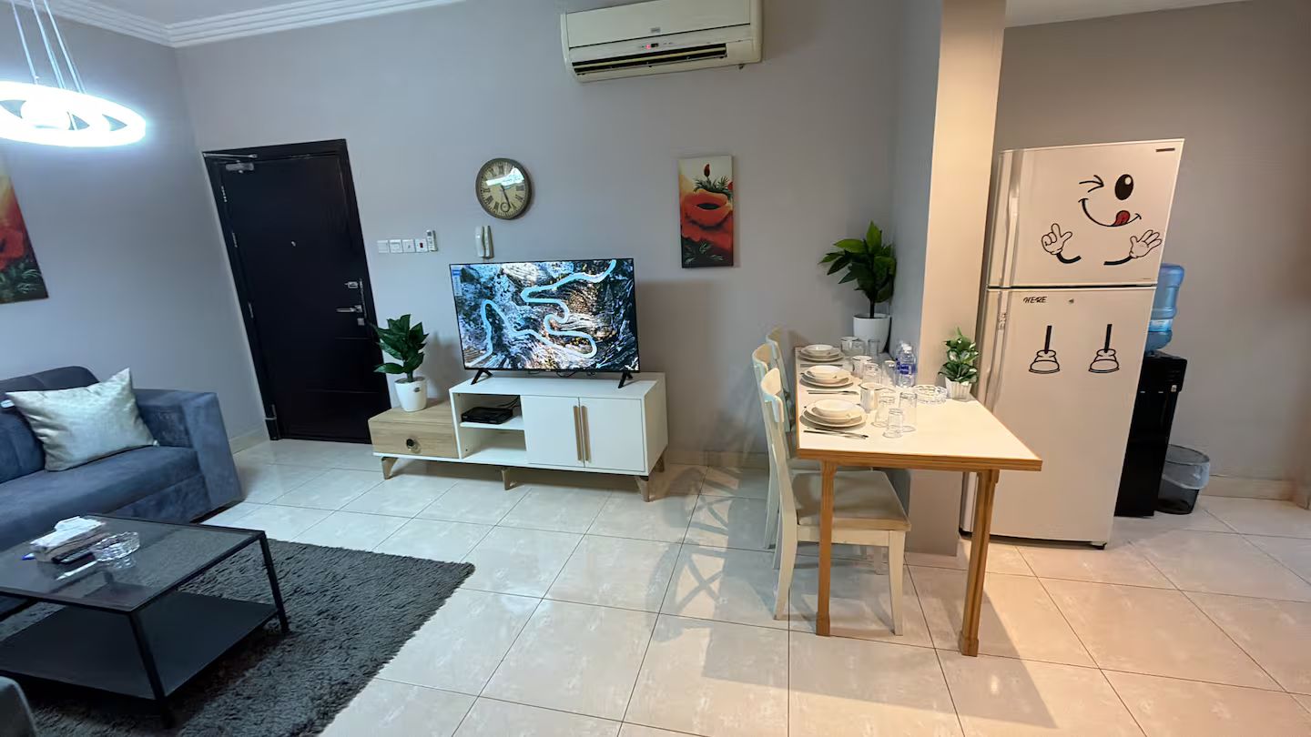 Una sala de estar moderna con sofá, mesa de centro, televisor y un comedor con mesa y sillas.