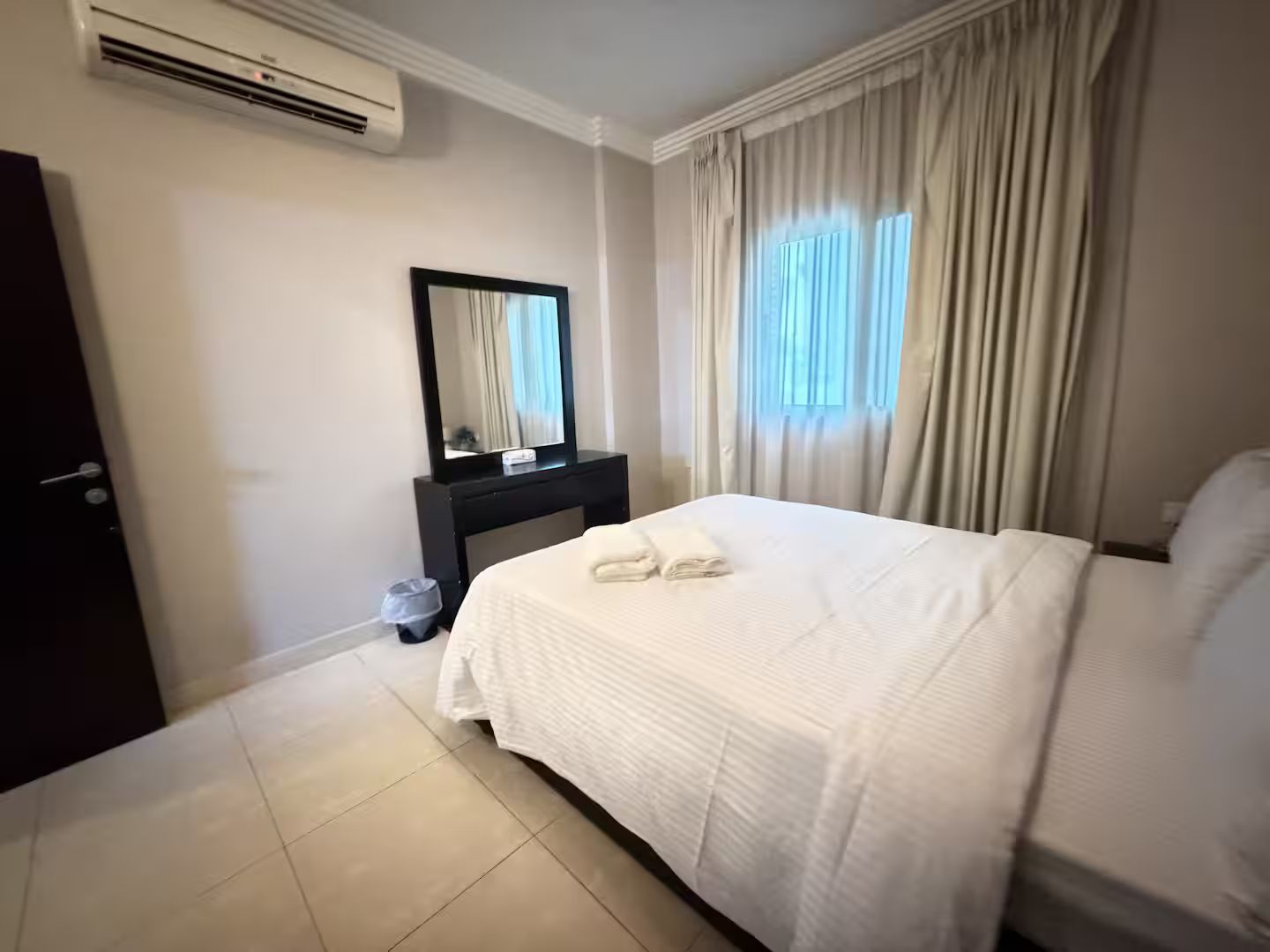 Una habitación de hotel con una cama, un aparador, un espejo y un equipo de aire acondicionado.