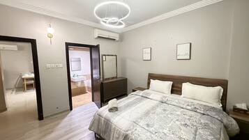 A bedroom with a bed, bedside tables, a mirror, and an air conditioning unit.