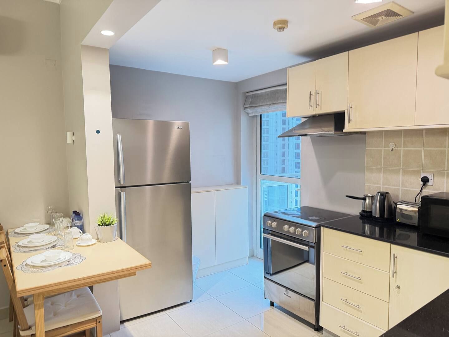 A modern kitchen with stainless steel appliances, a dining table set for four, and a view of the city through the window.