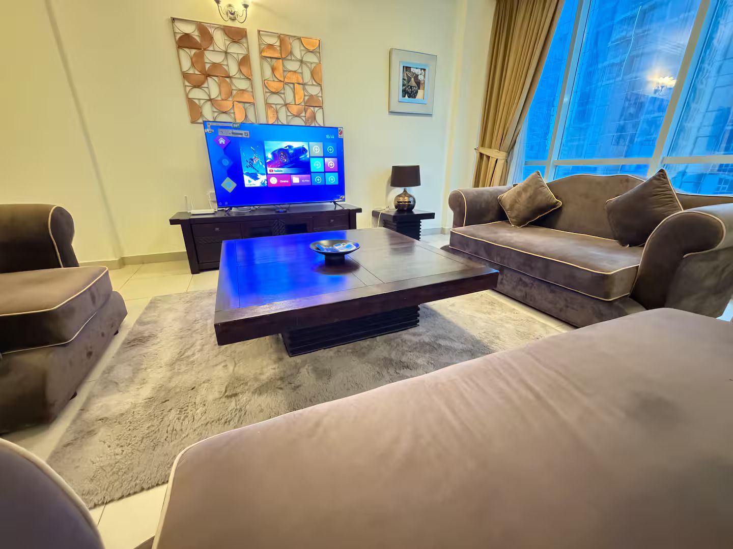 A modern living room with a flat-screen TV, a dark coffee table, and a brown sofa.