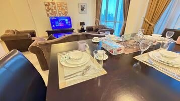 Un comedor con una mesa preparada para cuatro personas, un televisor al fondo y vistas de la ciudad a través del ventanal.