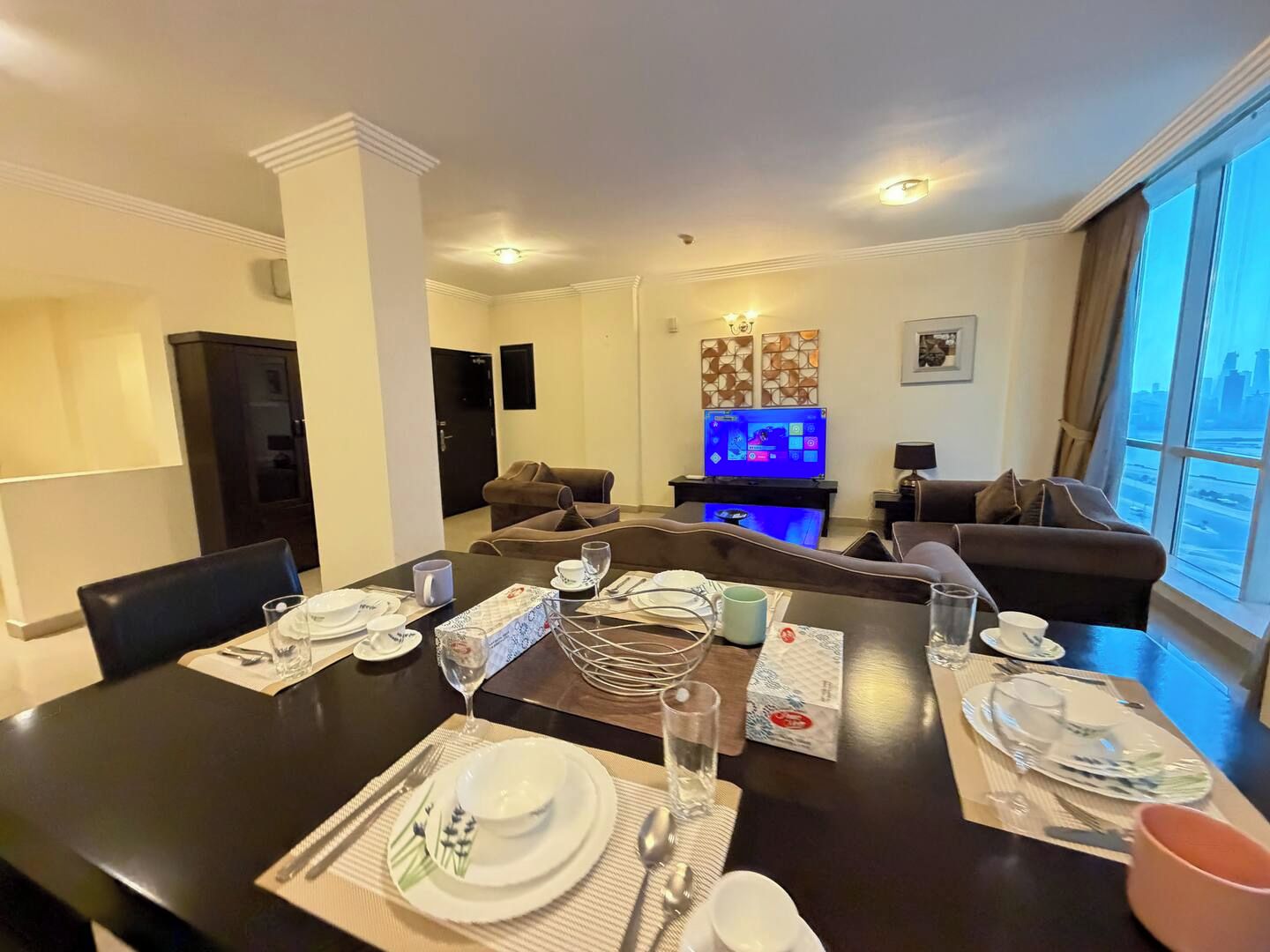Una sala moderna con comedor, televisor de pantalla plana y un ventanal con vistas a la ciudad.