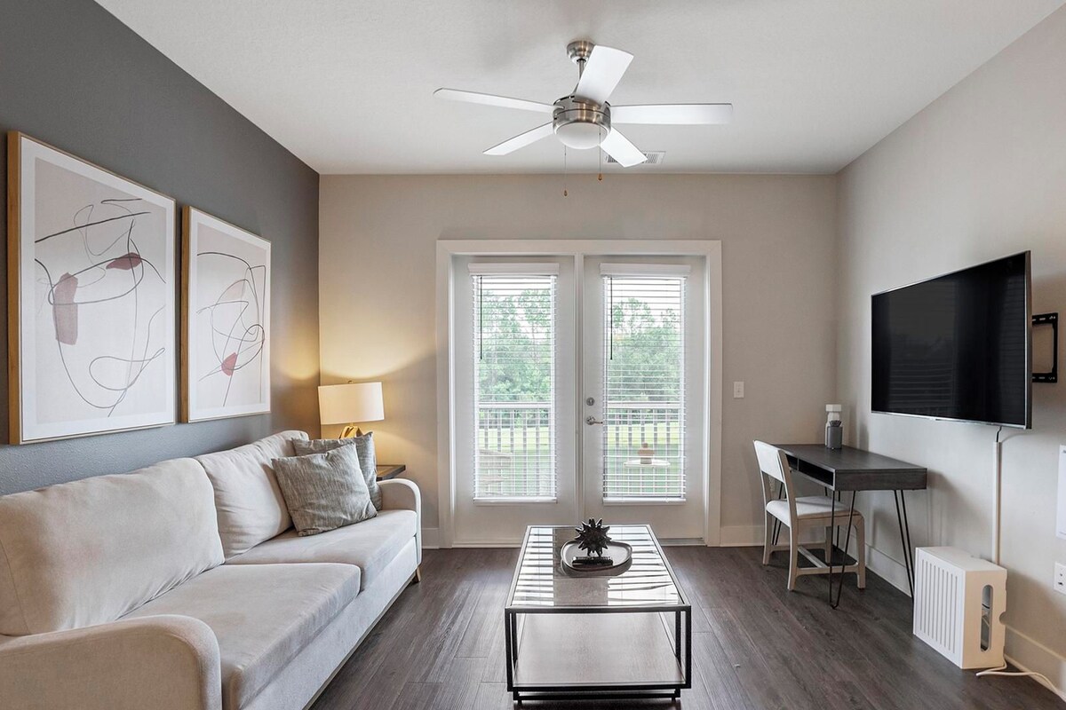 A living room with a ceiling fan, a sofa, a coffee table, a TV, and a door with blinds.