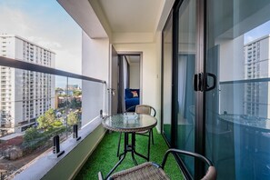 Ein Balkon mit Glastisch und -stühlen, einem blauen Sofa und Blick auf Stadtgebäude.