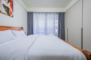 Ein Hotelzimmer mit einem großen Bett, einem Holzkopfteil, einem Gemälde an der Wand und Blick ins Freie durch transparente Vorhänge.
