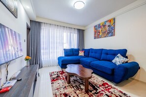 Ein modernes Wohnzimmer mit einem blauen Modulsofa, einem Couchtisch, einem Flachbildfernseher und einem Gemälde an der Wand.