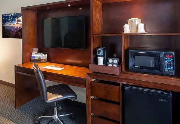 Ein Hotelzimmer mit einem Holztisch, einem Flachbildfernseher, einer Kaffeemaschine, einer Mikrowelle und einem kleinen Kühlschrank.