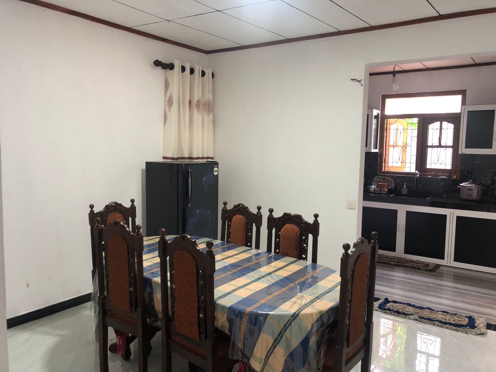 Un comedor con mesa y sillas, un refrigerador y una zona de cocina con armarios y ventana.