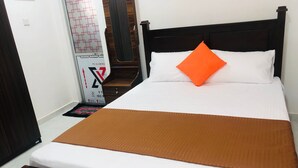 Een net opgemaakt bed met een bruine deken en een oranje kussen, een houten hoofdbord en een klein houten nachtkastje met een lamp.