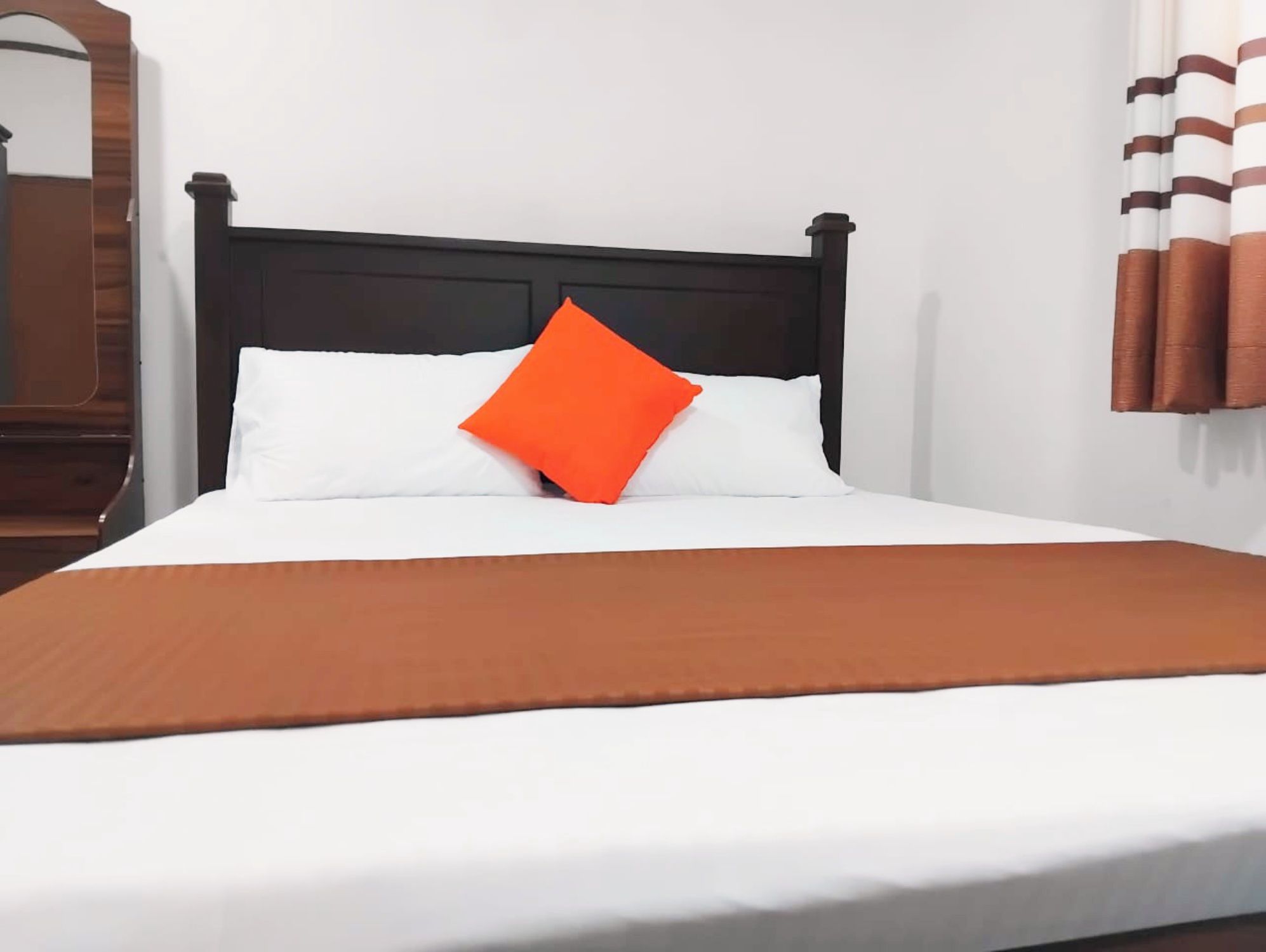 Un lit avec une tête de lit noire, une literie blanche et un oreiller orange.