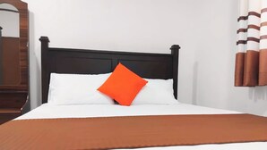 Een bed met een zwart hoofdeinde, witte beddengoed en een oranje kussen.