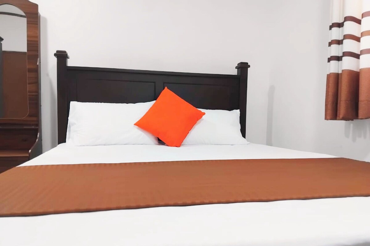 Ein Bett mit schwarzem Kopfteil, weißer Bettwäsche und einem orangefarbenen Kopfkissen.