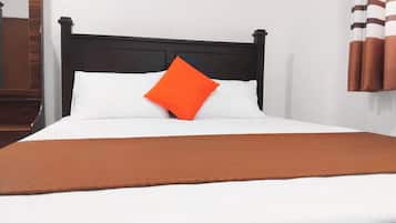Un lit avec une tête de lit noire, une literie blanche et un oreiller orange.
