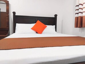 Ein Bett mit schwarzem Kopfteil, weißer Bettwäsche und einem orangefarbenen Kopfkissen.