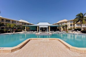 Una piscina con zona techada, sillones de descanso y cielo despejado.