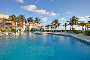 Un espace piscine d’hôtel avec une eau d’un bleu limpide, des chaises longues et des palmiers.
