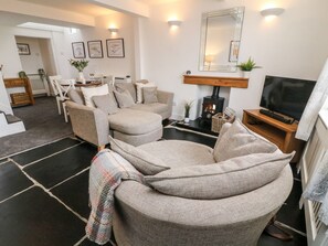 A living room with a sofa, a fireplace, a television, and a dining area with chairs and a table. - Crag Cottage (Settle)