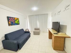 A living room with a sofa, a television, a small table, and a painting on the wall. - Marupiara Muro Alto (Ipojuca)