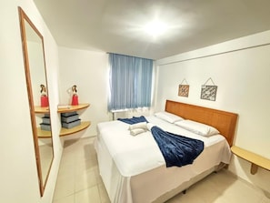 A hotel room with a bed, a mirror, a window with curtains, and a small shelf with items. - Marupiara Muro Alto (Ipojuca)