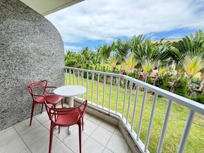 A balcony with a round table and red chairs, surrounded by a white railing, overlooking a garden with various plants and a clear sky. - Marupiara Muro Alto (Ipojuca)