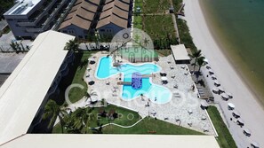 An aerial view of a resort with a large pool area, multiple lounge chairs, and a beach adjacent to the property. - Marupiara Muro Alto (Ipojuca)